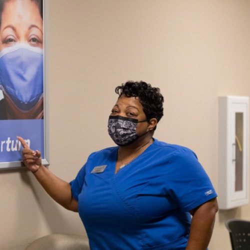 healthcare worker in max pointing to sign with her face on it