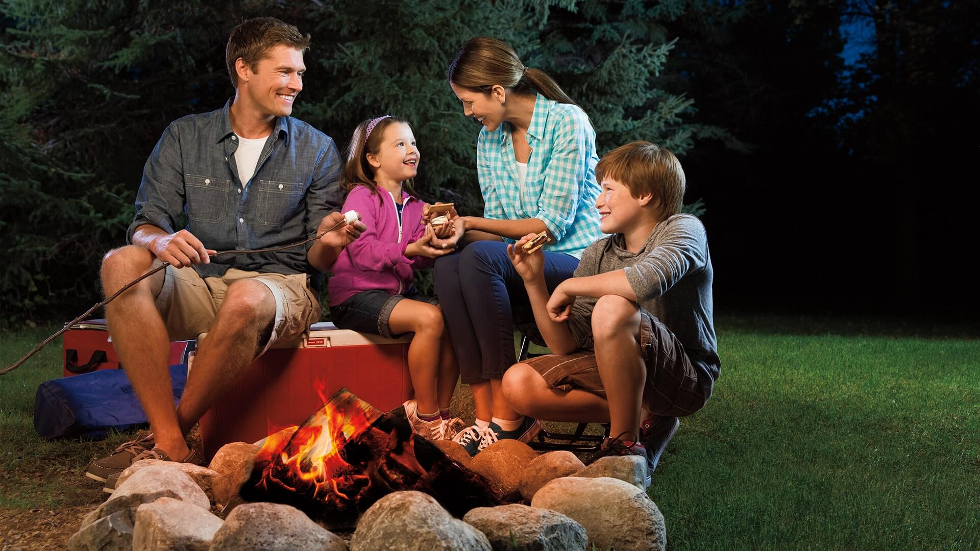 family sitting around a campfire while making smores