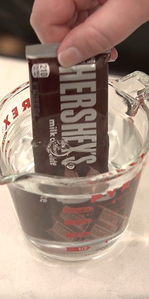 person melting a fully wrapped hersheys milk chocolate candy bar in hot water