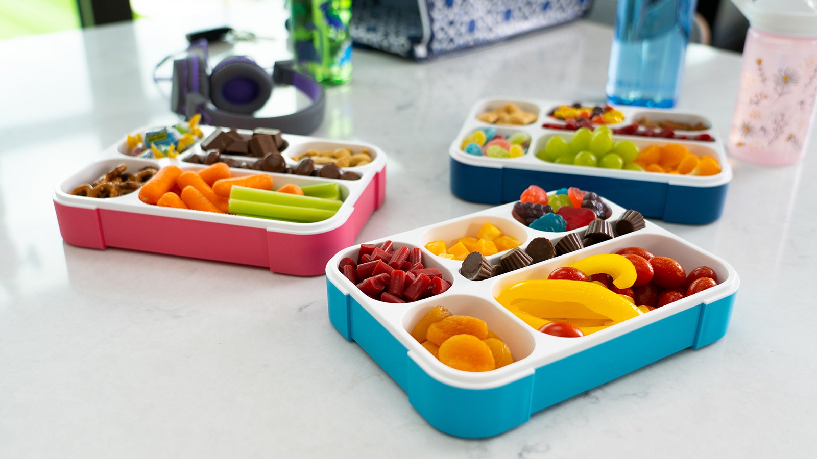 three bento boxes filled with candy, fruit and snacks