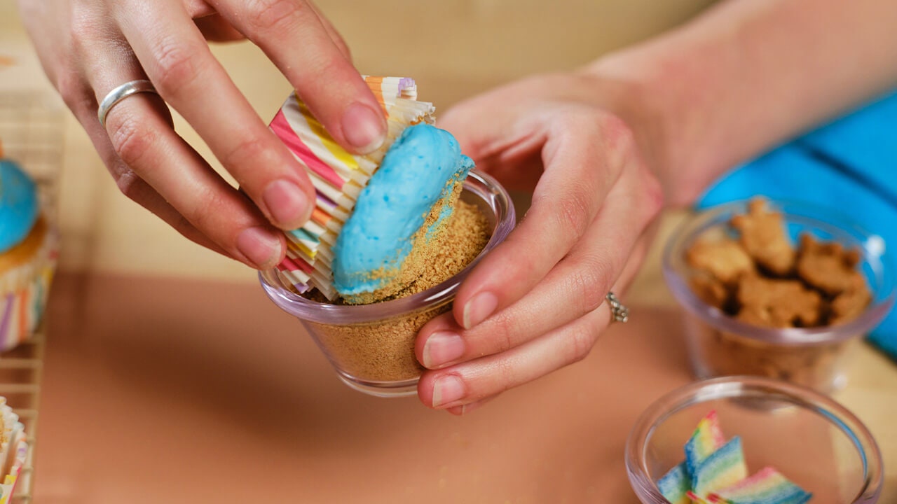 person dipping cupcake top into graham cracker crumbs