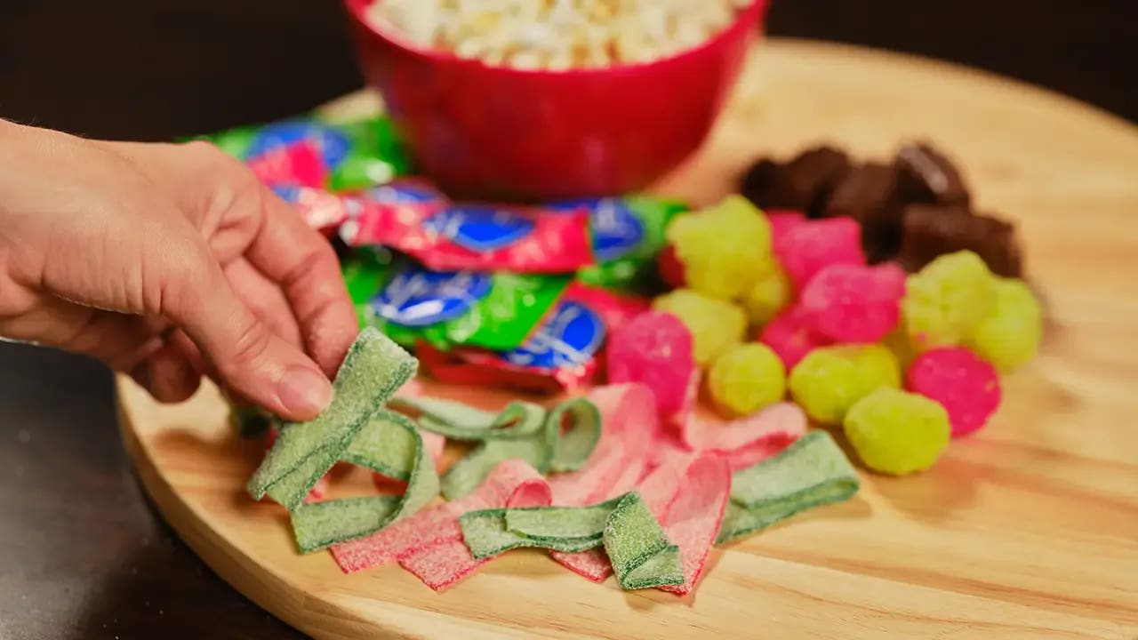 A hand holding sour strips over the candy board