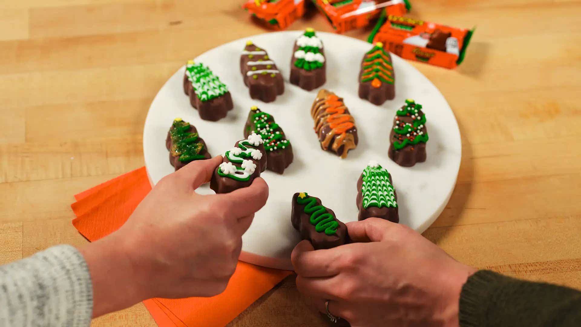 hands picking up decorated reeses trees from a marble board