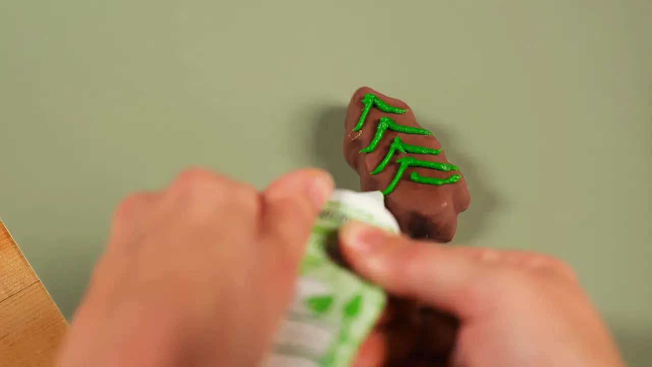 hand piping green icing onto a reeses tree