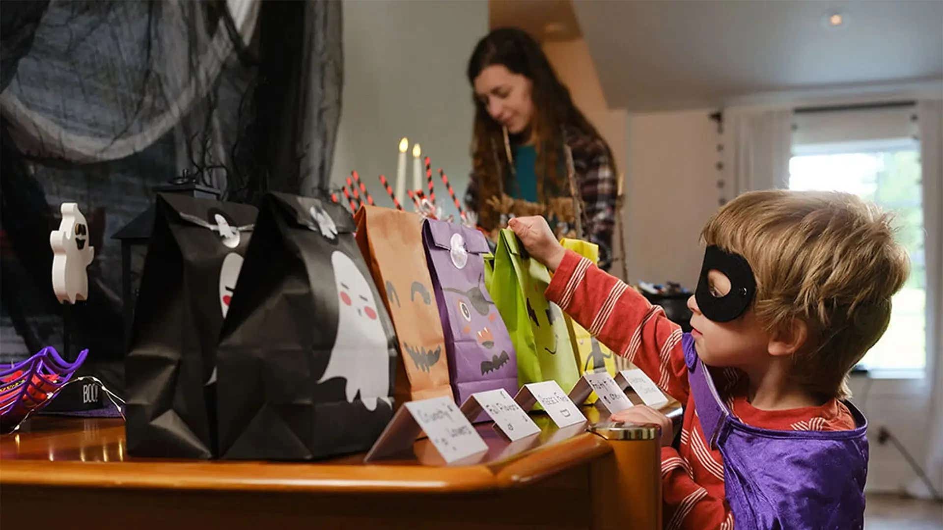 child dressed up in a halloween costume taking a treat bag from the table