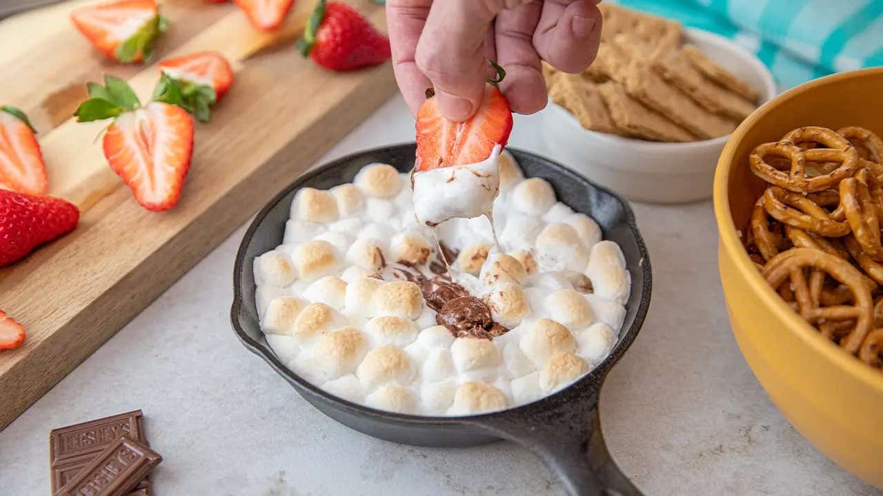person dipping strawberry into smores skillet dip
