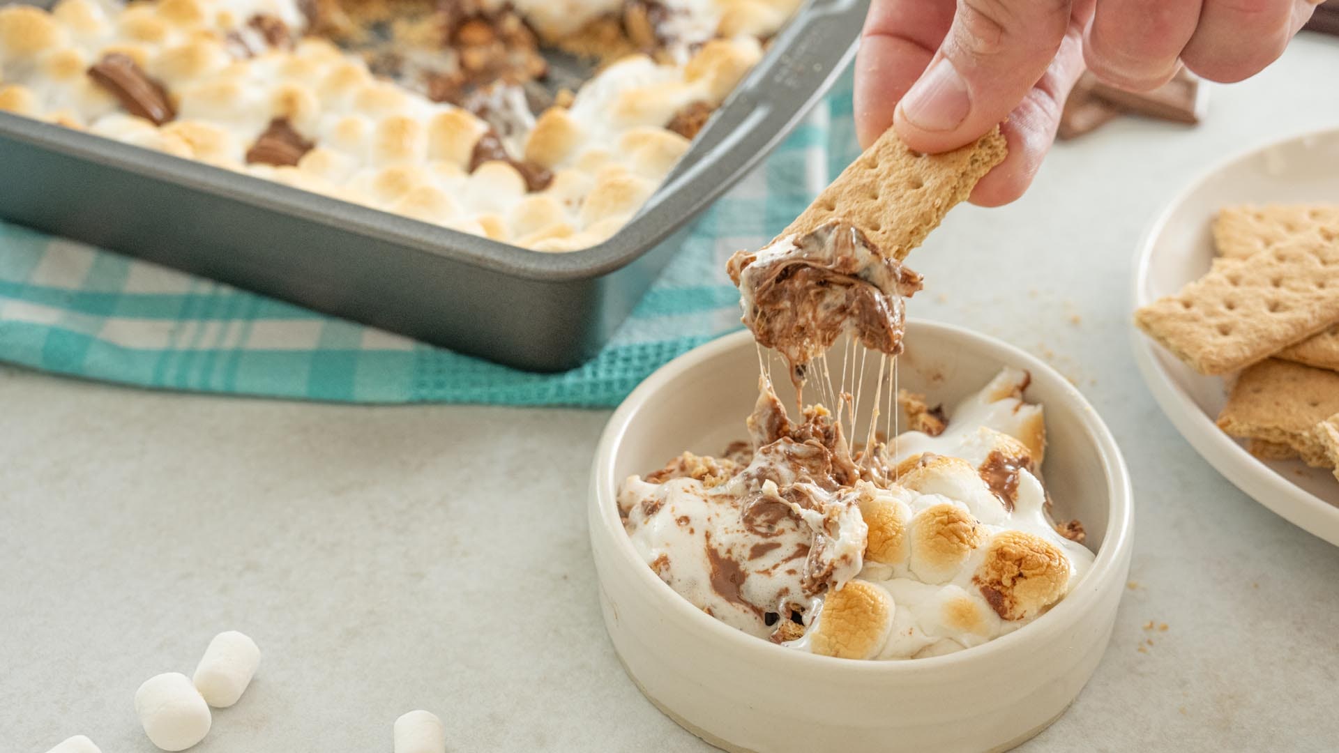 dipping into bowl of smores smash with graham cracker