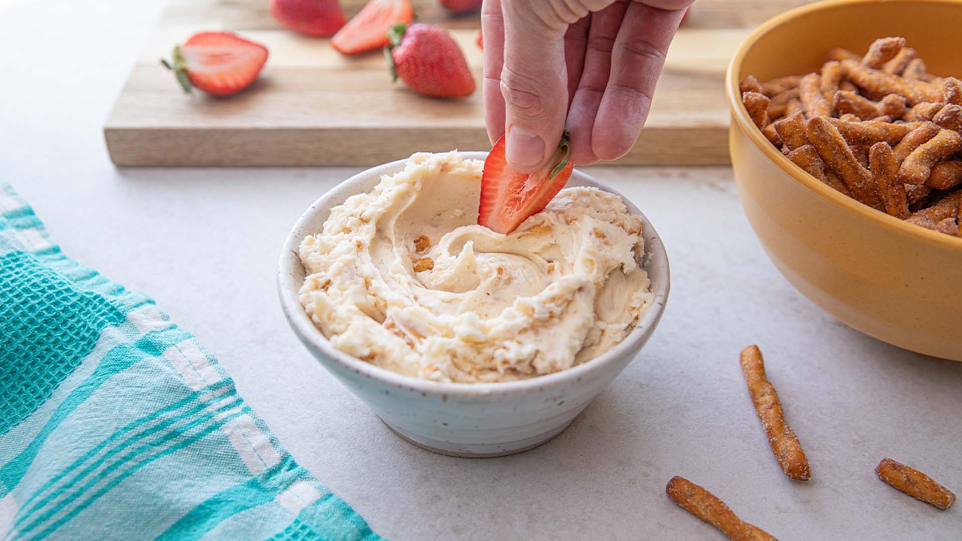 person dipping a strawberry into the dots cheesecake dip