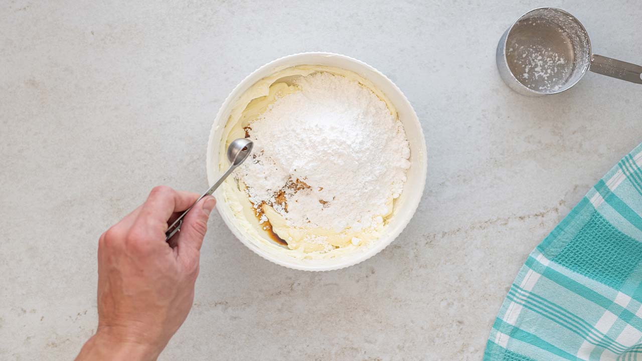person adding powdered sugar and vanilla into the bowl