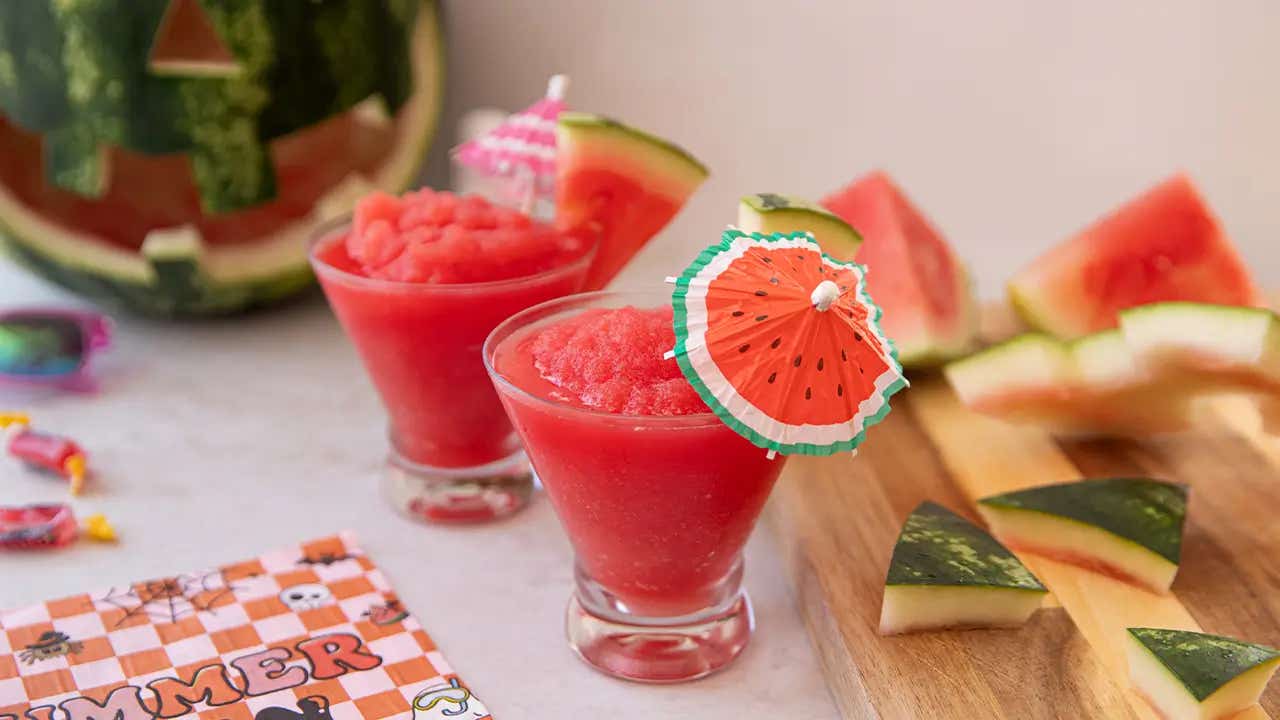 two glasses of watermelon slushie by cutting board with watermelon rind