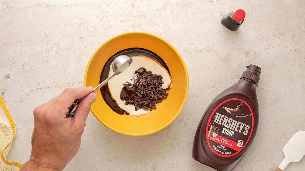 person adding chocolate chips, syrup and creme into a mixing bowl