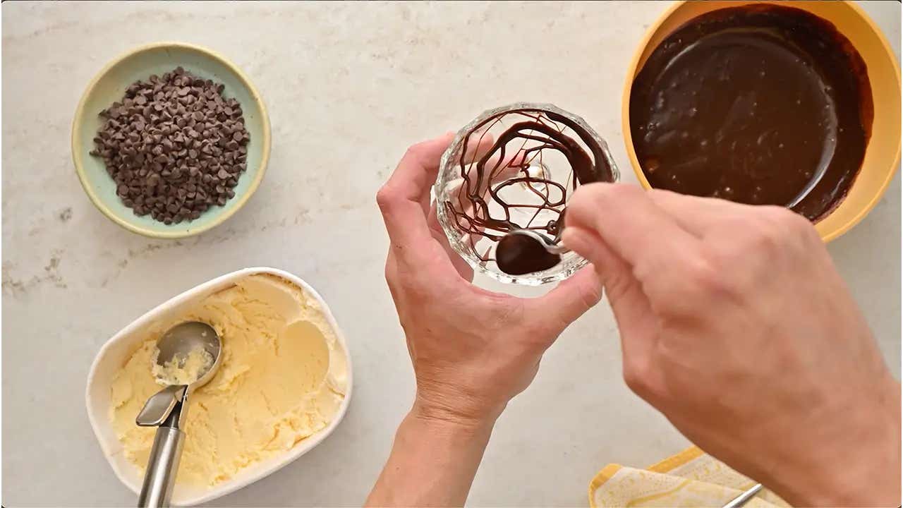 person drizzling chocolate sauce on the edges of a glass dessert cup