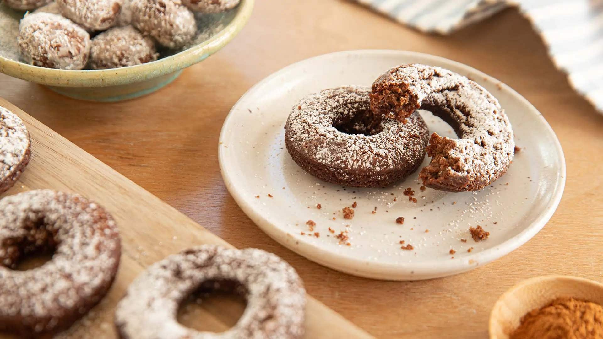 spiced cocoa doughnuts dusted with powdered sugar on plate with bitten doughnut