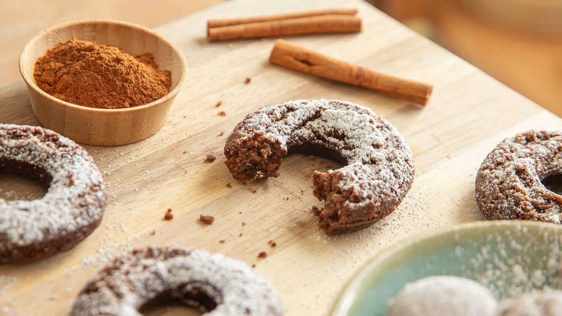 bitten spiced cocoa doughnut on wooden board with ground cinnamon and cinnamon sticks