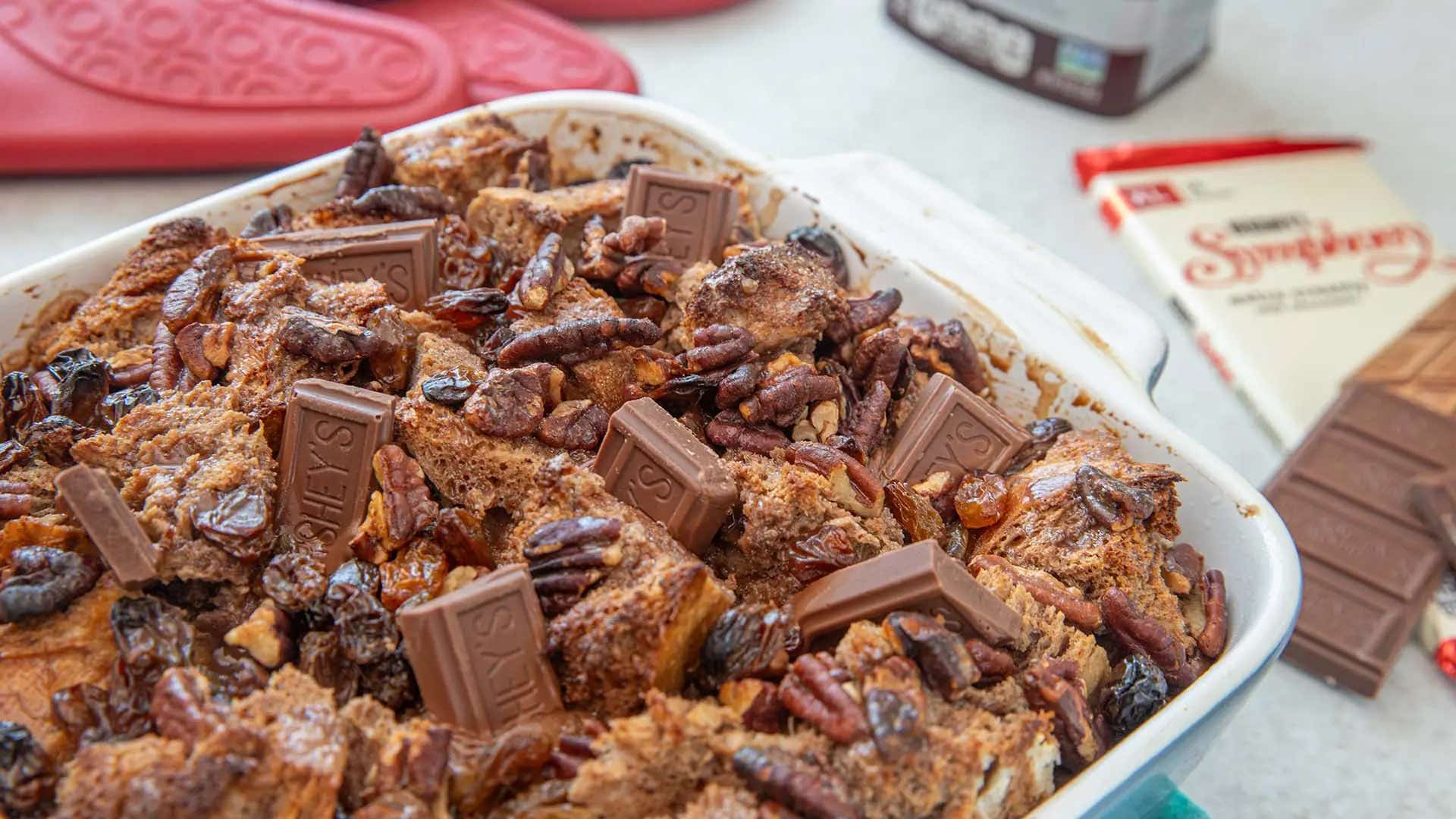 chocolate bread pudding topped with pecans, raisins and milk chocolate pieces in a casserole dish