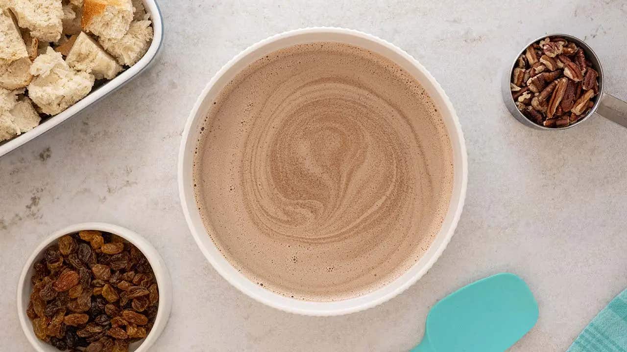 blended chocolate milk mixture in bowl with raisins and pecans nearby
