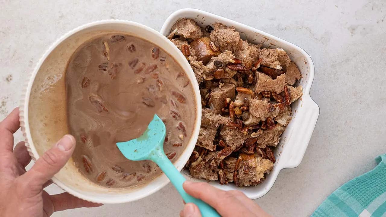 pouring chocolate mixture with pecans over bread in casserole dish