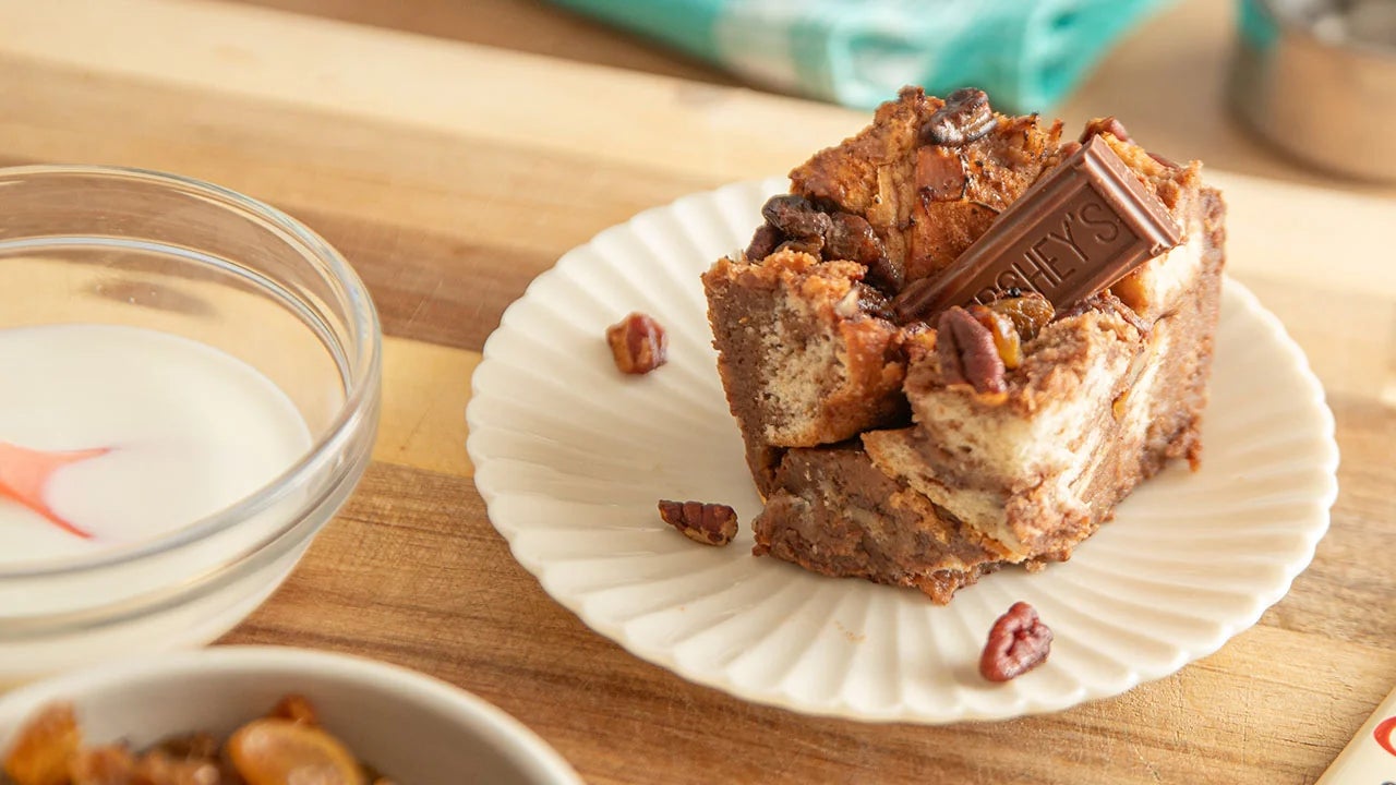 serving of chocolate bread pudding topped with milk chocolate piece beside bowl of cream
