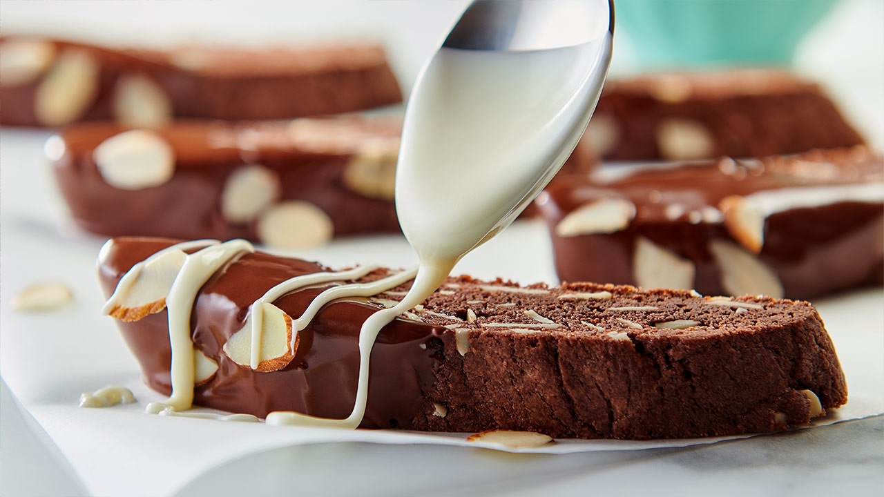 drizzling white glaze on top of a biscotti