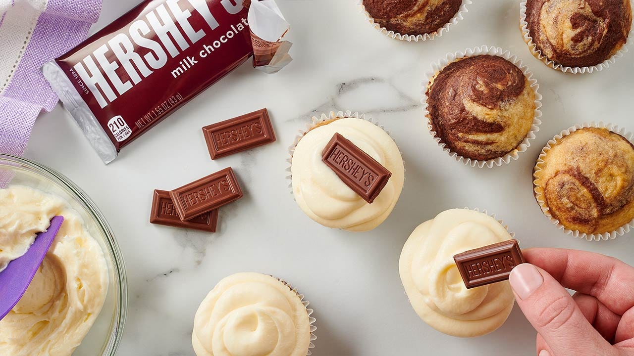 person adding marshmallow frosting and a hersheys pip to each smores cupcake