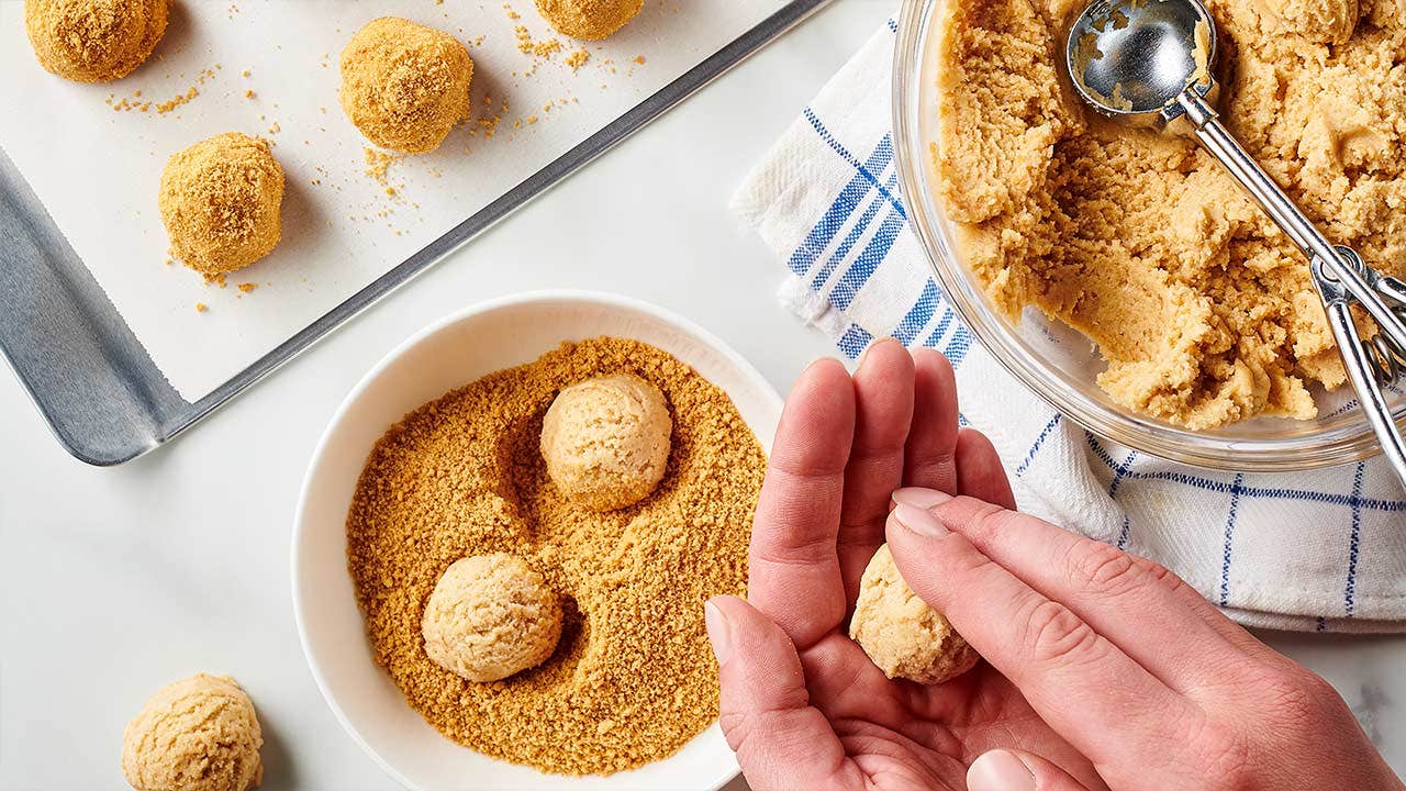person rolling dough into balls and rolling them through bowl of graham cracker crumbs