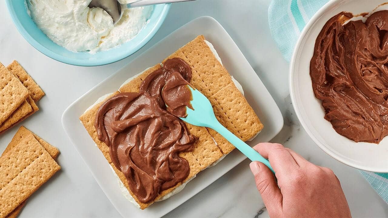 person spreading chocolate pudding on top of graham cracker sheets