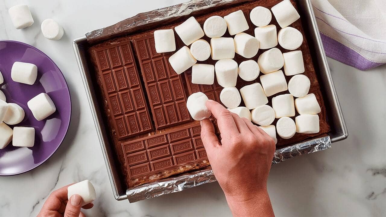 person adding marshmallows on top of hersheys milk chocolate bars 