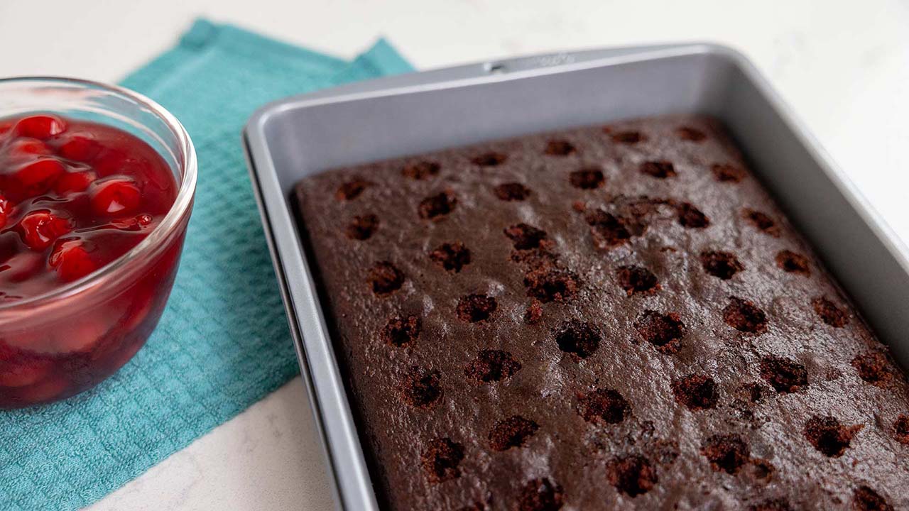 adding cherry filling to the pan of the black forest poke cake