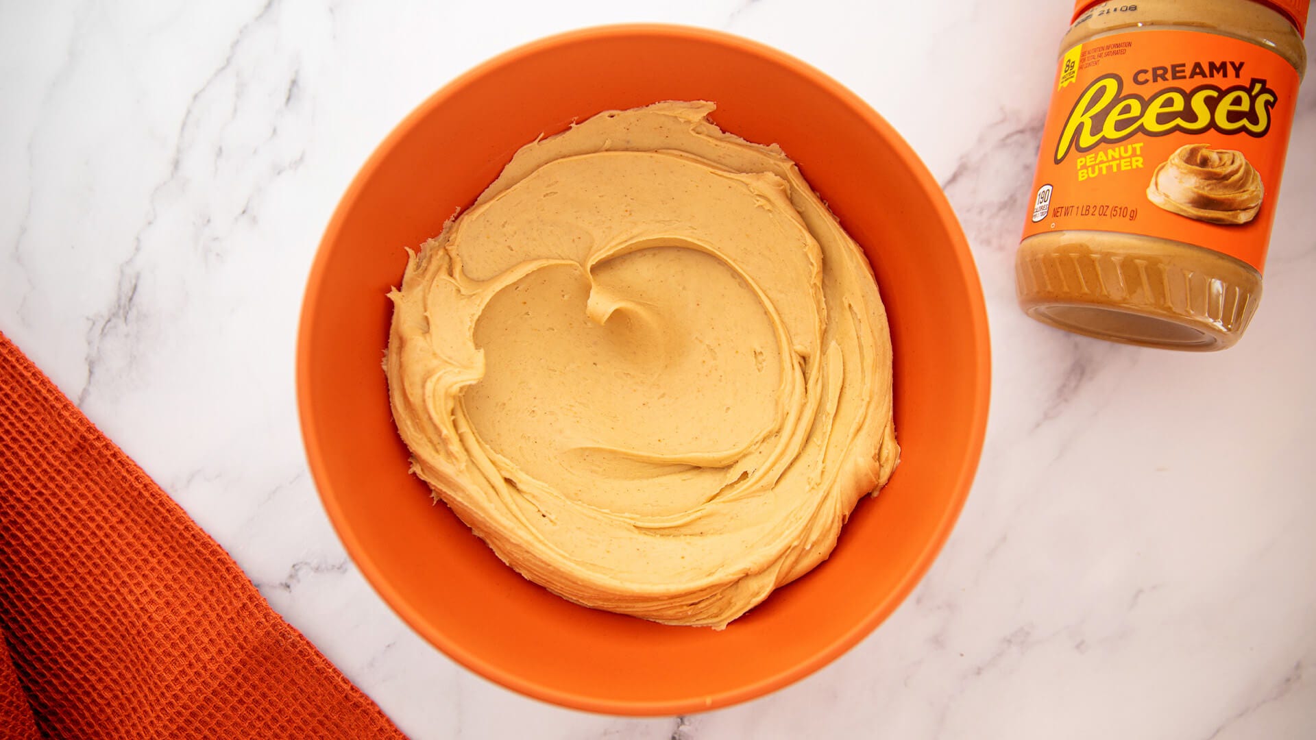 mixing bowl filled with reeses peanut butter frosting beside a jar of reeses peanut butter