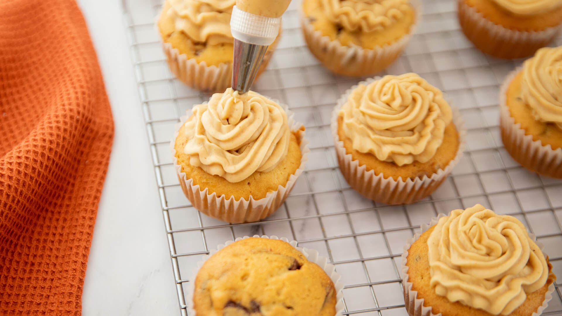 reese's peanut butter frosting being piped over vanilla cupcakes