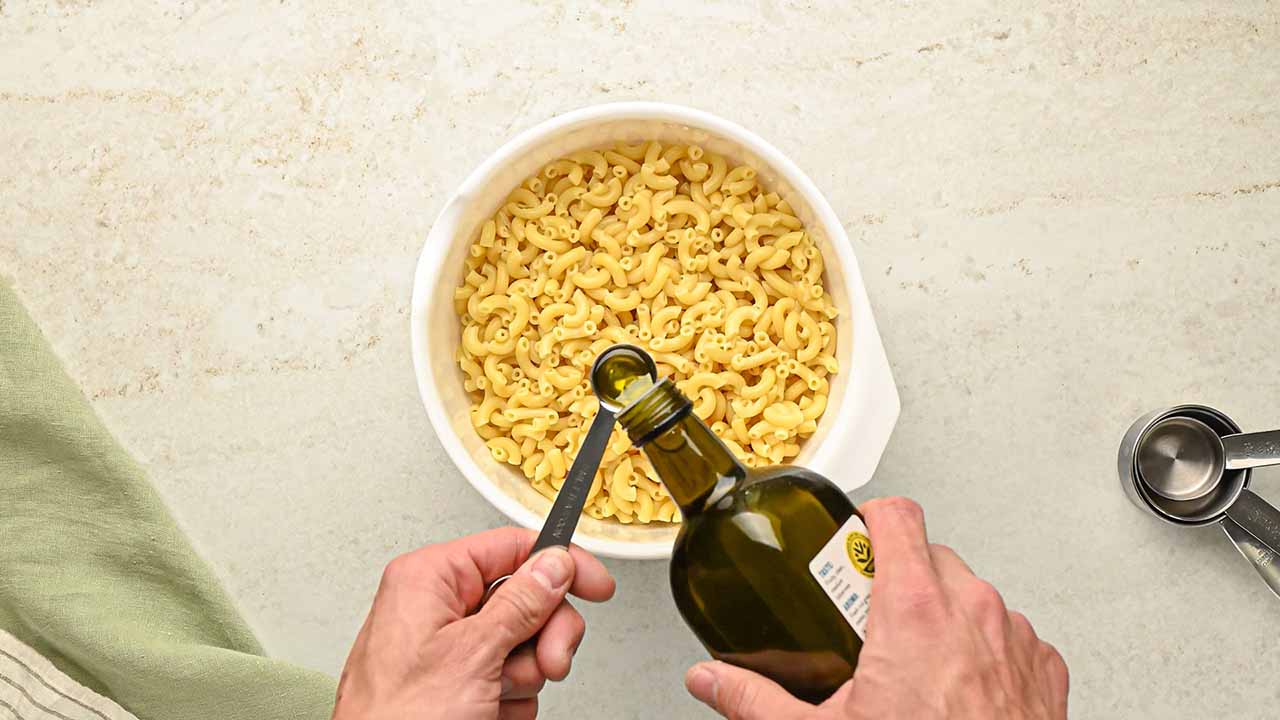 adding and mixing the olive oil into the fully cooked macaroni