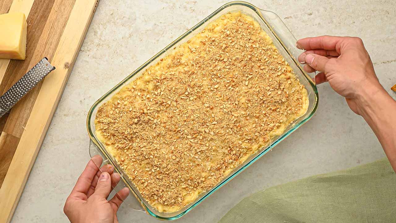 pouring the macaroni into a baking dish and topping with pretzel crumbs and parmesan cheese