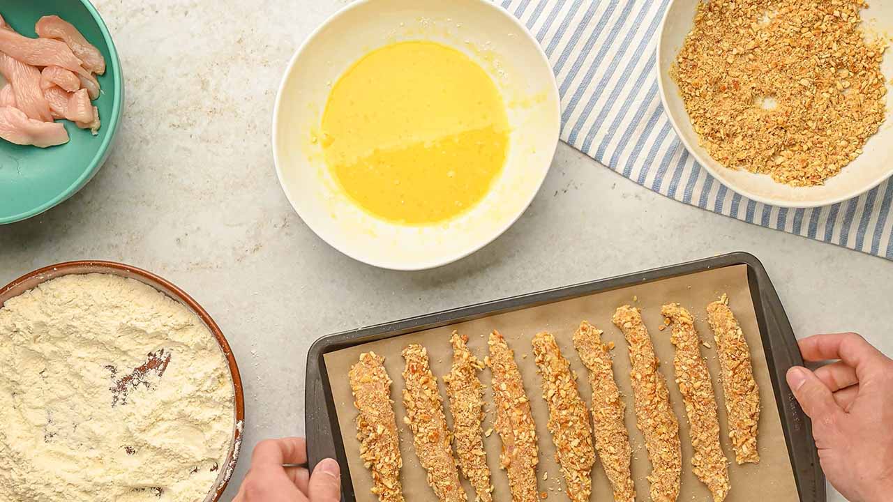 coating the chicken strips with pretzel crumbs and placing them onto a baking sheet