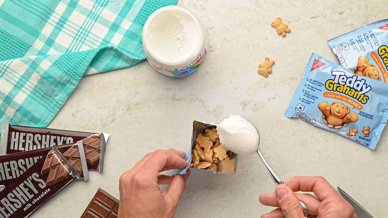 person adding spoonful of marshmallow creme into teddy grahams bag