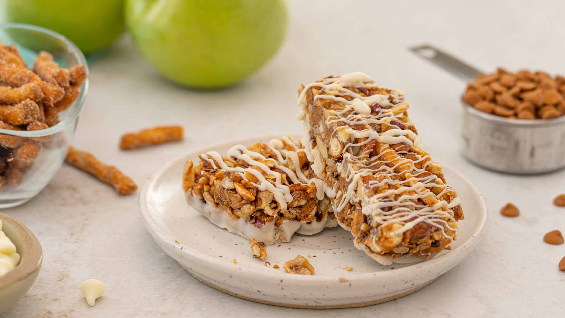 plate of dots apple cinnamon nut bars beside bowls of pretzels, baking chips, and apples