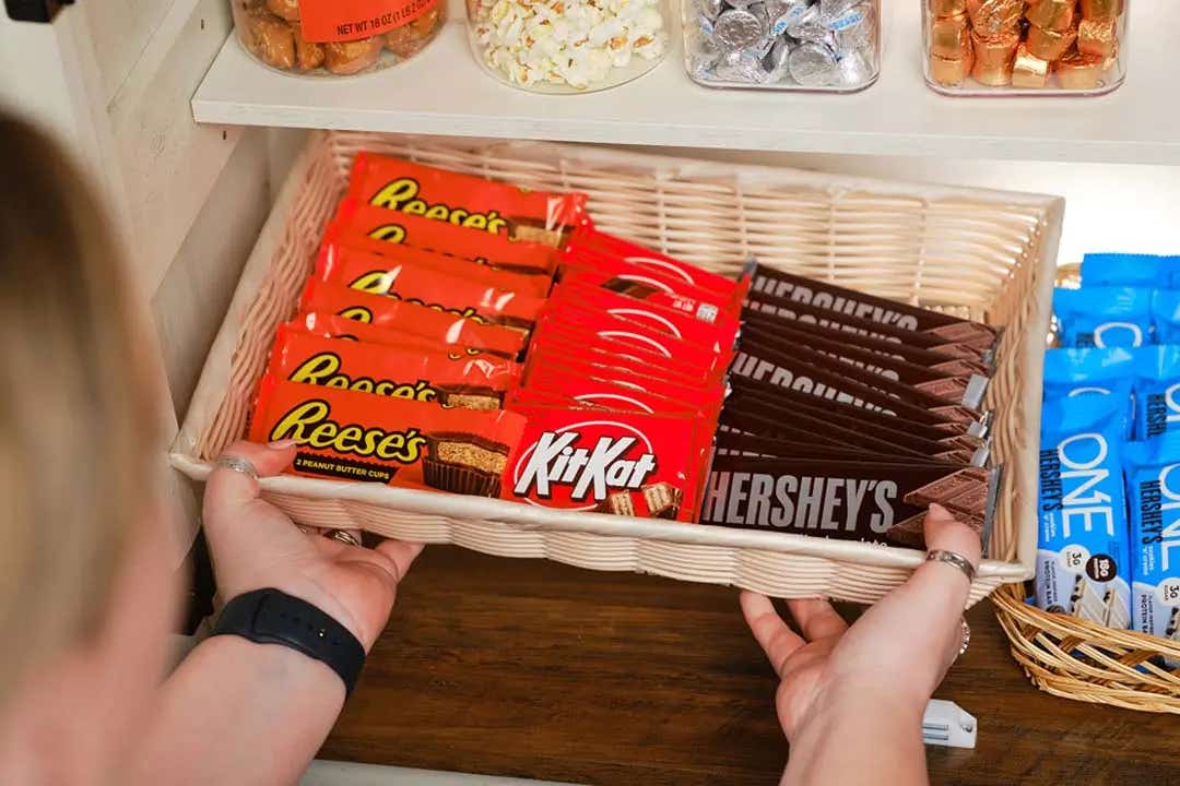person grabbing a basket of assorted hersheys candy bars from pantry