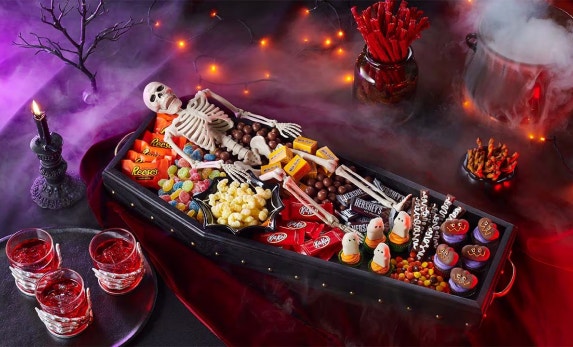 halloween themed table decorated to look like a graveyard with coffin shaped candy dish filled with hersheys candy