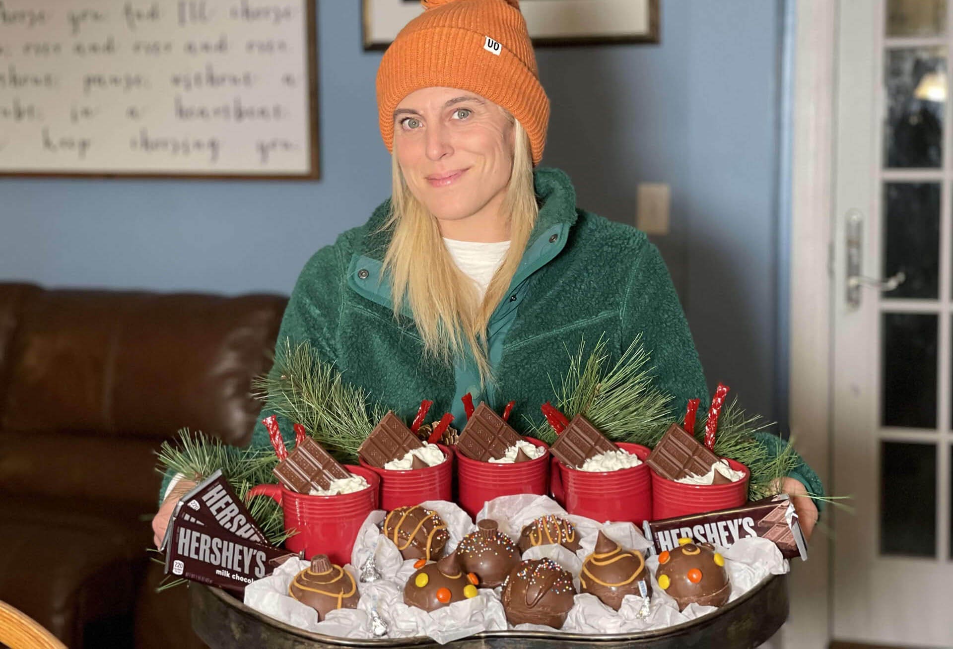 Influencer sitting behind tray of hot cocoa bombs and full mugs
