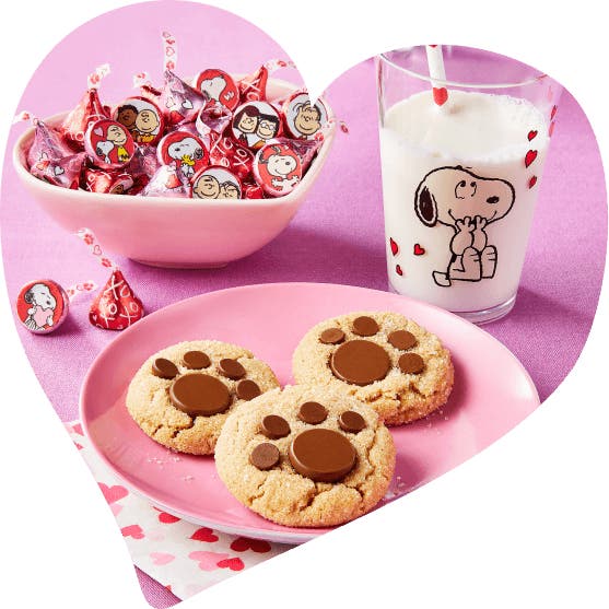 plate of paw print cookies  on table with bowl of snoopy hershey kisses and a glass of milk