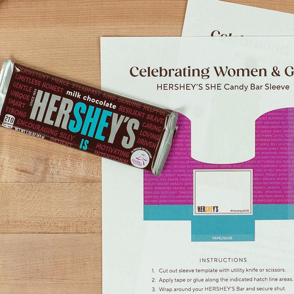 Printable candy bar sleeve craft shown with scissors, tape and HERSHEY’S SHE Candy bars