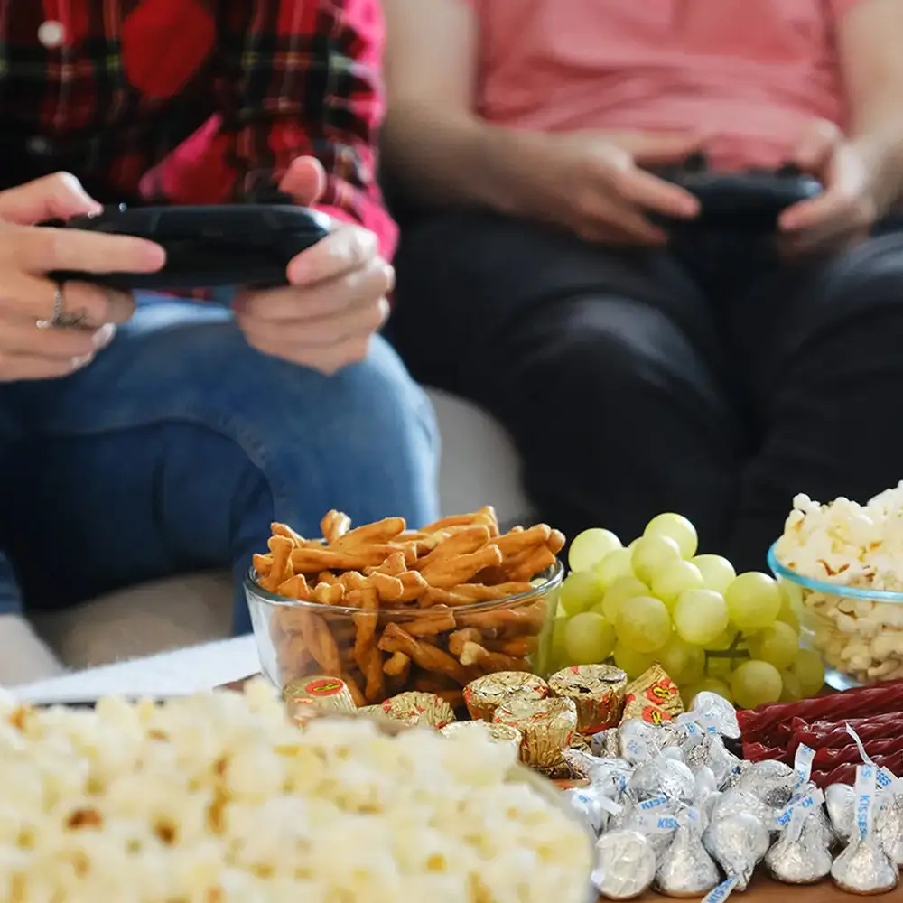 people playing videogames in front of table full of snacks
