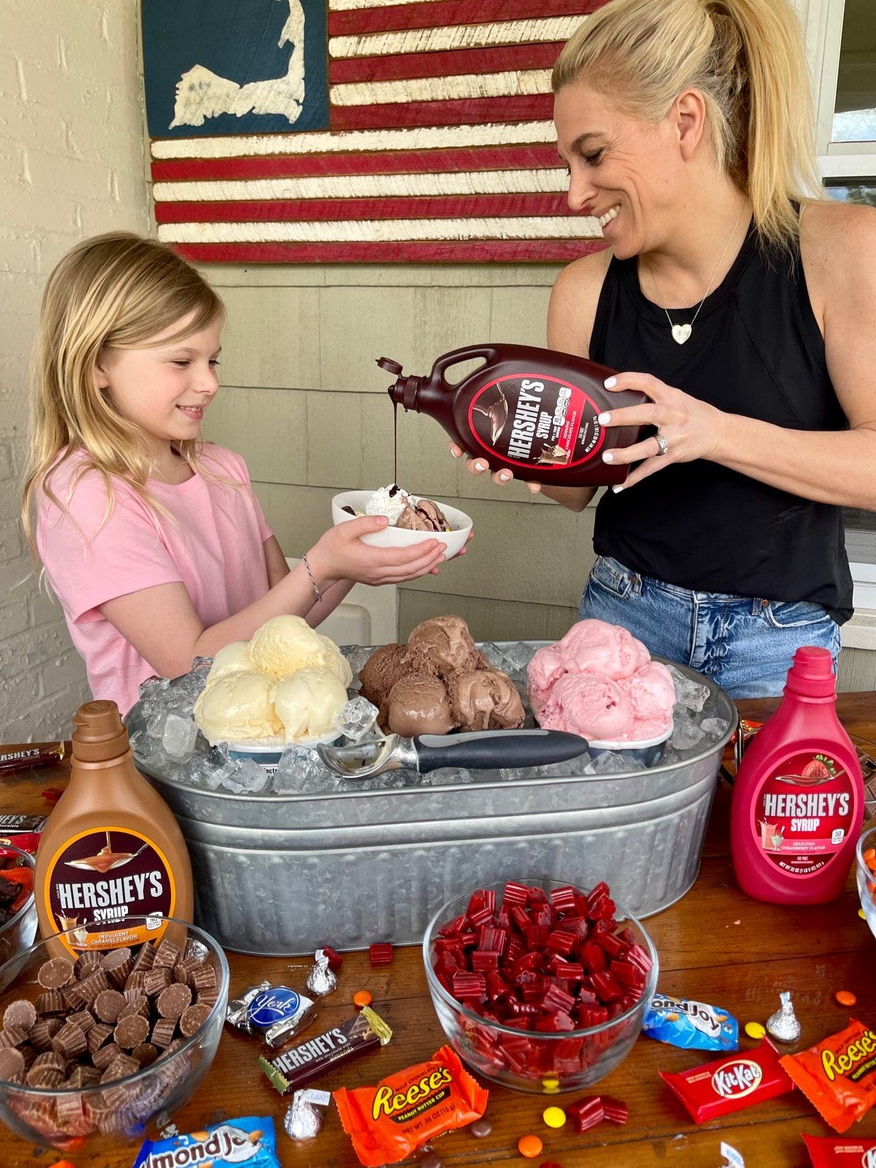 mother pouring hershey syrup on young daughter's sundae
