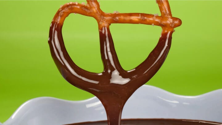 pretzel being dipped in chocolate