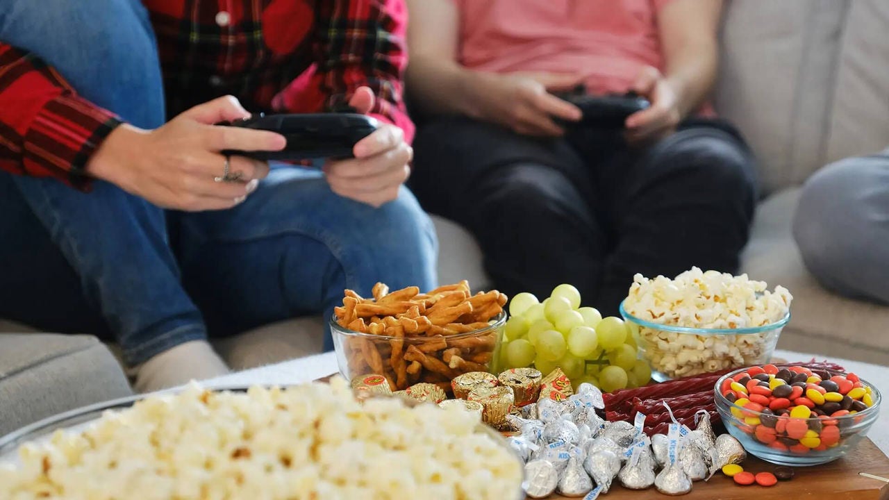 snacks on coffee table while people play video games on the couch