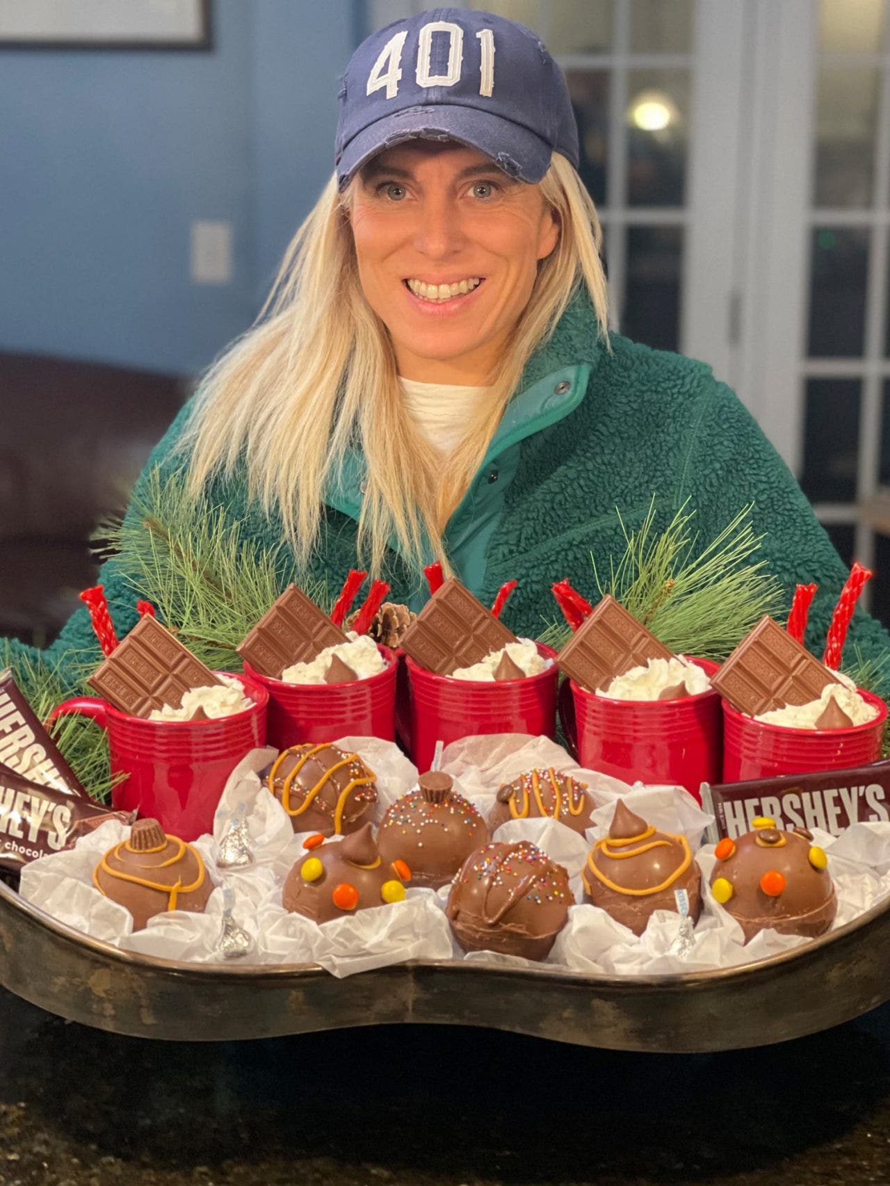 influencer holding a tray of hot cocoa bombs alongside mugs of hot chocolate