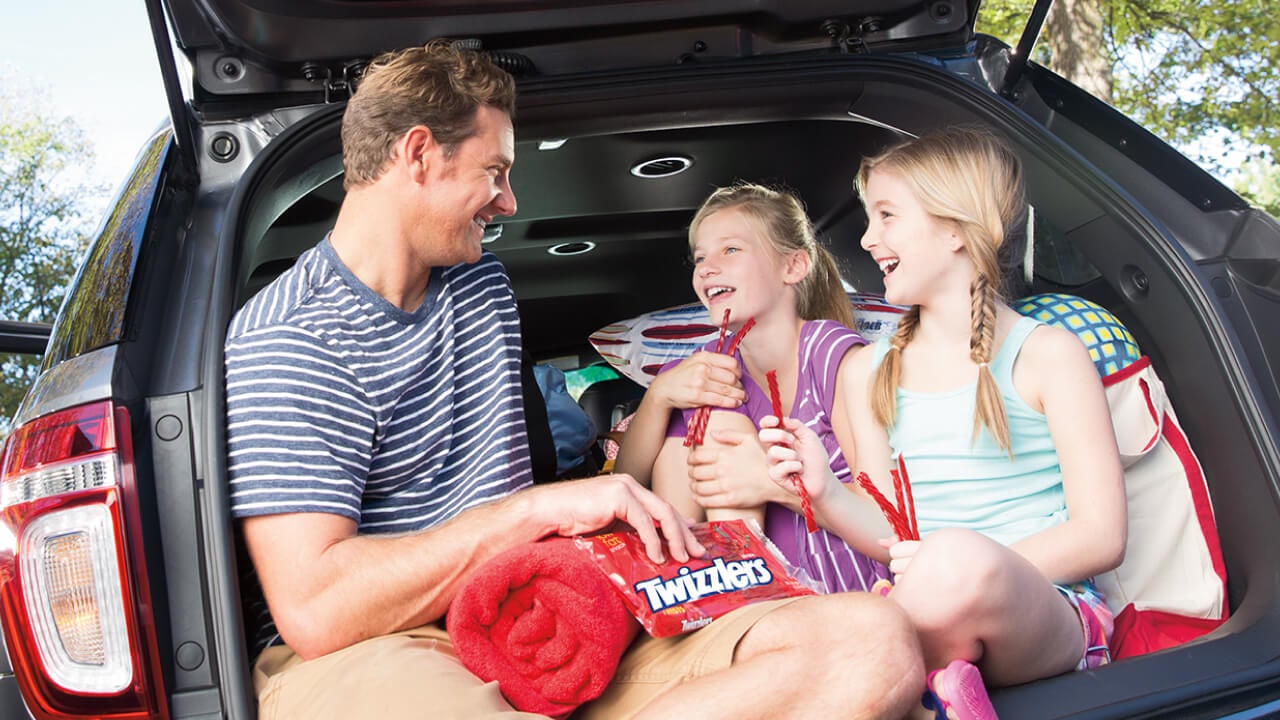 father and two daughters sitting in the trunk of a car eating twizzlers